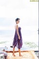 A woman standing in front of a window looking out at the ocean.