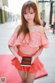 A woman in a pink top and orange skirt holding a tablet.