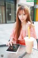 A woman sitting at a table with a tablet and a drink.