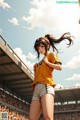 A woman in a yellow shirt and white shorts standing in front of a crowd.