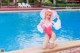 A woman in a pink bathing suit and hat by a swimming pool.