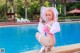 A woman in a pink bikini and hat sitting by a swimming pool.