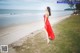 A woman in a red dress walking on the beach.