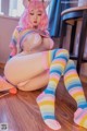 A woman with pink hair sitting on the floor wearing colorful stockings.