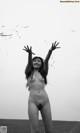 A naked woman standing in a field with her arms outstretched.