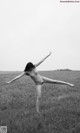 A naked woman standing in a field with her arms outstretched.