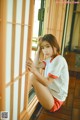 A young woman sitting on a wooden floor next to a window.