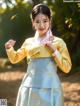 A woman in a yellow and blue hanbok poses for a picture.