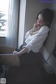 A woman wearing glasses sitting on a desk next to a window.