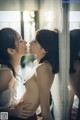 A couple of women standing next to each other near a window.