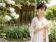 A woman in a white robe standing in front of a tree.