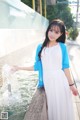 A woman in a white dress and blue cardigan standing next to a fountain.