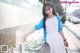 A woman in a white dress and blue cardigan standing next to a fountain.