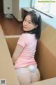 A woman in a pink shirt is sitting in a cardboard box.