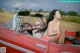 A woman sitting in the back seat of a red convertible car.