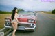 A woman standing next to a red car on the side of the road.