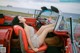 A woman sitting in the back seat of a red car.