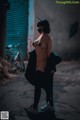 A naked woman wearing a mask standing in an alleyway.