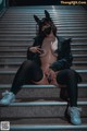 A woman wearing a cat mask sitting on some stairs.