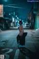 A woman in a cat mask is sitting on the street at night.