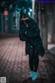 A woman wearing a black cat mask standing on a cobblestone street.