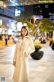 A woman in a white trench coat standing on a city street.