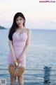 A woman in a pink dress standing on a pier by the water.