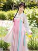 A woman in a pink and blue hanbok standing in a garden.