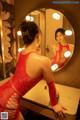 A woman in a red bodysuit looking at herself in the mirror.