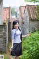 A woman in a blue shirt and black skirt standing in a garden.