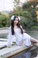 A woman in a white dress sitting on a ledge by a pond.