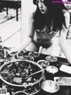 A naked woman sitting at a table with a large pot of food.