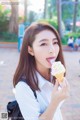 A woman eating an ice cream cone in a park.