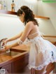 A woman in a white dress is washing her hands in a kitchen sink.